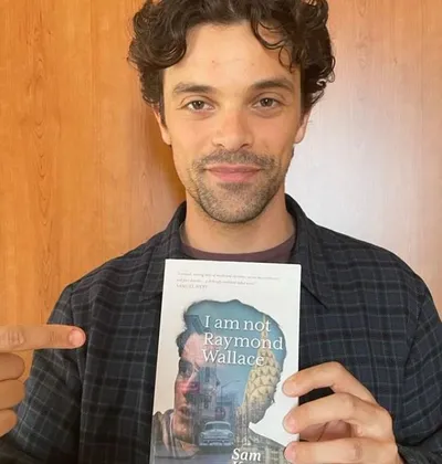 Jacob Fortune-Lloyd wearing a black shirt showing the book "i am not raymond wallace"