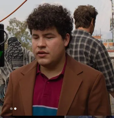 Actor Alexis Ojitos de Huevo wearing a maroon T-shirt and brown jacket