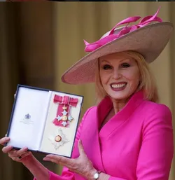 Joanna Lumley in a pink suit and hat, proudly holds a medal, showcasing her achievement and success.