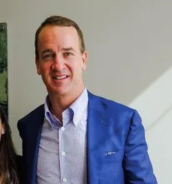 Peyton Manning is wearing a blue jacket with a white shirt.