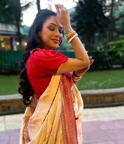 Rupali Ganguly wearing a red and white sari, standing gracefully with a serene expression on her face.