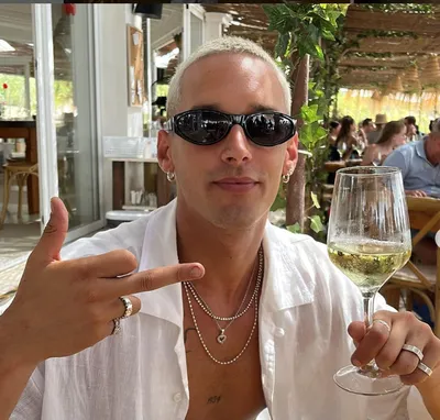 actor Joel Sánchez  wearing sunglasses holds a glass of wine, exuding an air of sophistication and relaxation.